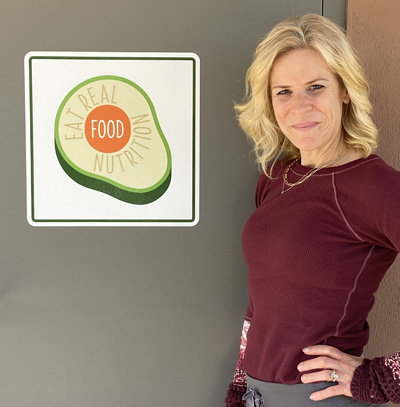 Molly Obert, Nutrition Consultant poising in front of the logo for her company Eat Real Food Nutrition